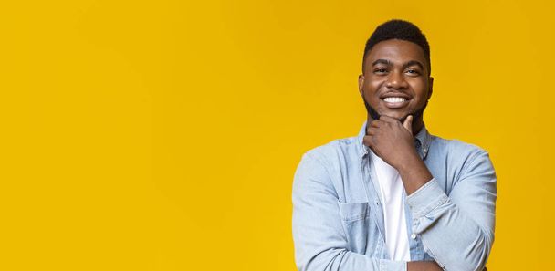 Smiling african guy touching his beard on yellow background - Photo, Image