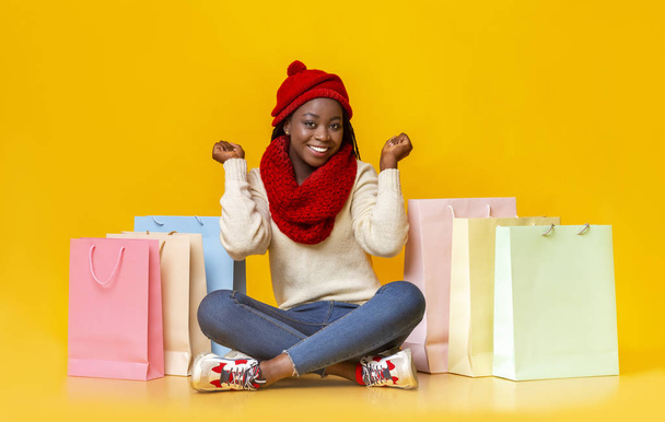 Emotional black girl in winter clothes sitting among shopping bags - Photo, Image