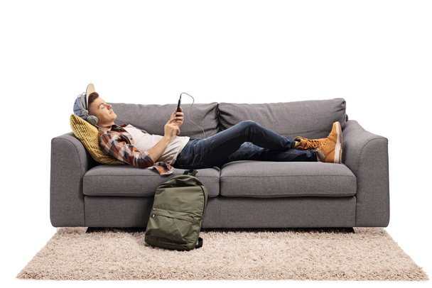 Teenage guy lying on a sofa and listening to music with headphon - Фото, зображення