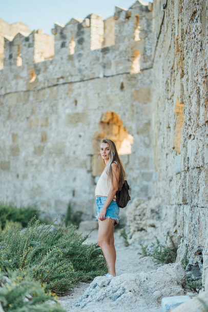 Beautiful young blonde hair girl traveler near the fort wall Rhodes island, Greece - Photo, image