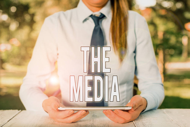 Writing note showing The Media. Business photo showcasing main means of mass communication that are regarded collectively Female business person sitting by table and holding mobile phone. - Photo, Image