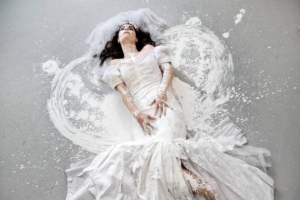 красивая молодая художественно абстрактно нарисованная женщина, невеста в свадебном платье с белой краской, абстрактное искусство тела, на полу в студии, копировальное пространство
. - Фото, изображение