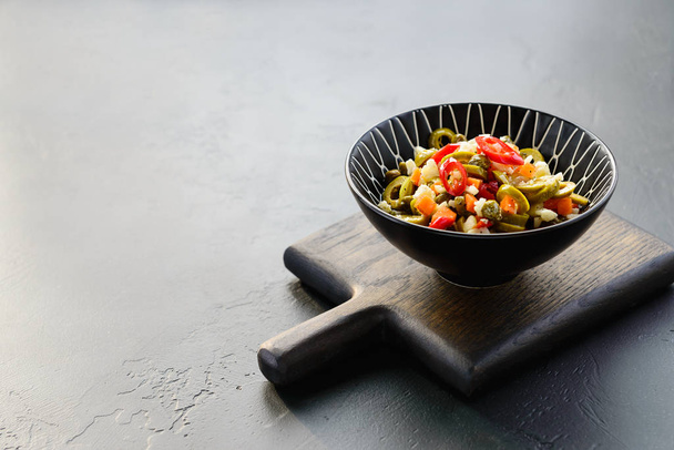 Olive salad for muffuletta in a bowl on a dark wooden board. Horizontal orientation, copy space. - Φωτογραφία, εικόνα