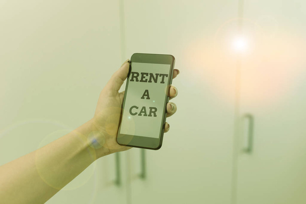 Pisanie notatki pokazującej Rent A Car. Business photo showcasing płacąc za tymczasowe korzystanie z pojazdu od jednego dnia do miesięcy kobieta za pomocą smartfona i urządzeń technologicznych wewnątrz domu. - Zdjęcie, obraz