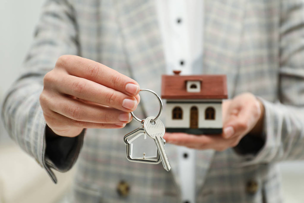 Real estate agent holding house model and key indoors, closeup - Photo, Image