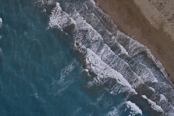 White foamy sea waves splash to deserted sandy beach in the evening. Evening surf. Aerial top view from UAV drone - Fotó, kép