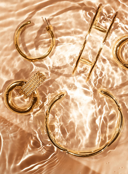 Golden bracelets, earrings, rings, jewelery on gold water backgr - Photo, Image
