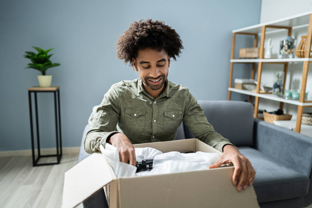 Smiling Young Man Sitting On Sofa Unpacking Received Parcel - Photo, image