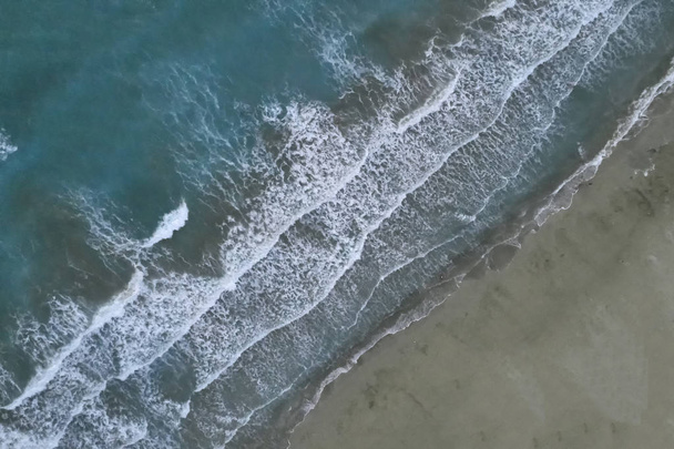 White foamy sea waves splash to deserted sandy beach in the evening. Evening surf. Aerial top view from UAV drone - Foto, imagen