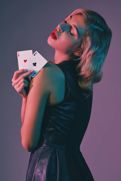 Ragazza bionda in abito elegante nero che mostra due carte da gioco, posa su sfondo colorato. Divertente gioco d'azzardo, poker, casinò. Primo piano. - Foto, immagini