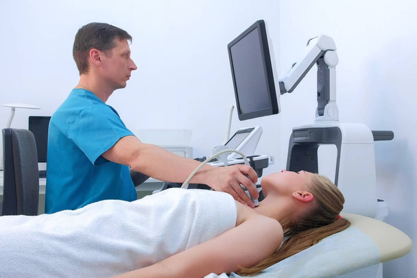 Doctor makes ultrasound scanning diagnostic of thyroid gland to woman in clinic. - Foto, afbeelding