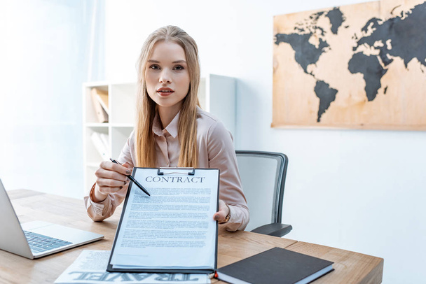 attractive travel agent pointing with pen at contract on clipboard - Photo, image