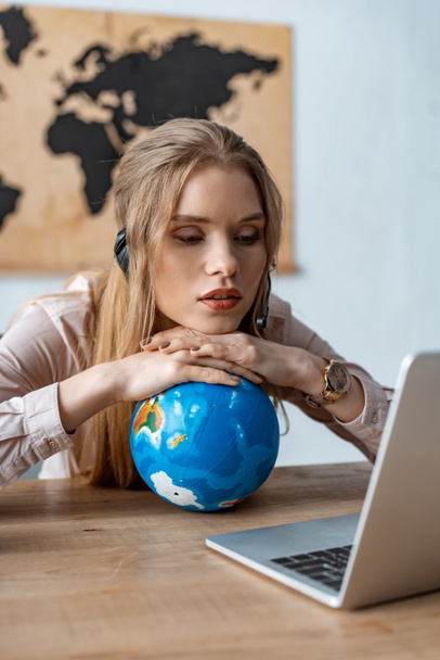 exhausted travel agent leaning on globe while looking at laptop - 写真・画像