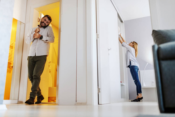 Young caucasian couple getting ready for work. Man getting out bathroom and talking on the phone while woman taking out clothes from wardrobe. - Foto, Imagen