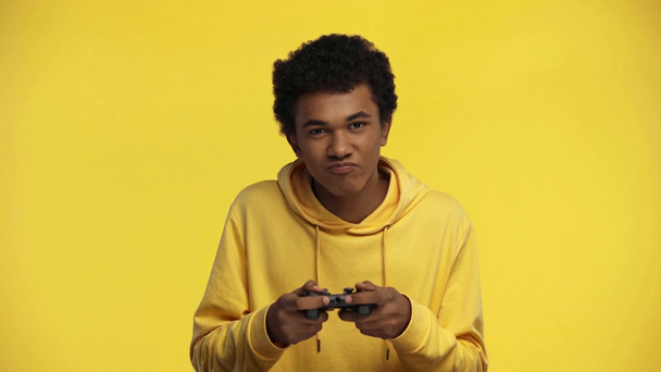 KYIV, UKRAINE - OCTOBER 18, 2019: african american teenager playing video game isolated on yellow - Materiał filmowy, wideo