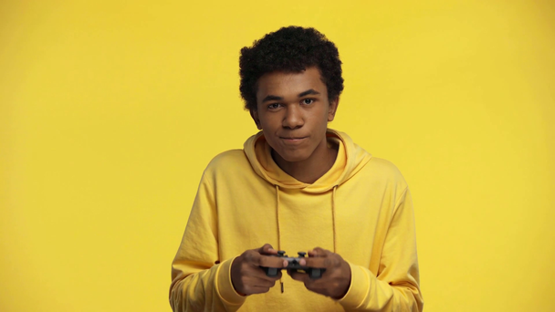 KYIV, UKRAINE LOKAKUU 18, 2019: afrikkalainen amerikkalainen teini, joka pelaa videopeliä eristettynä keltaisella
 - Materiaali, video