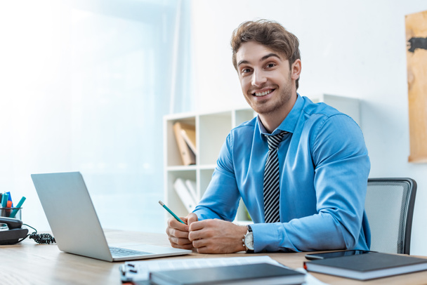 cheerful travel agent looking at camera while sitting at workplace - Photo, image
