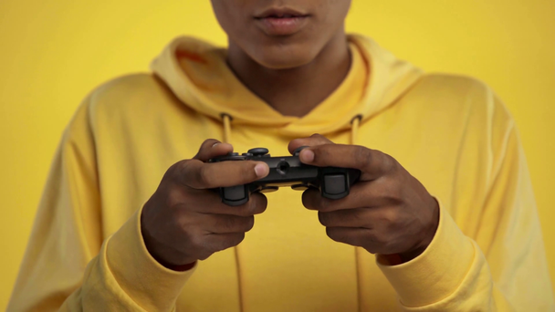 KYIV, UKRAINE - OCTOBER 18, 2019: cropped view of african american teenager playing video game isolated on yellow  - Footage, Video