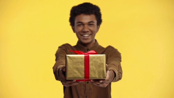 african american teenager holding gift isolated on yellow - Video, Çekim