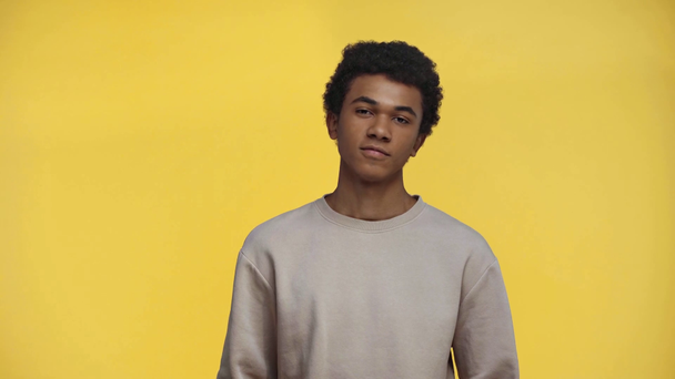 Αφροαμερικάνος έφηβος χαμογελά στην κάμερα απομονωμένος στο κίτρινο - Πλάνα, βίντεο