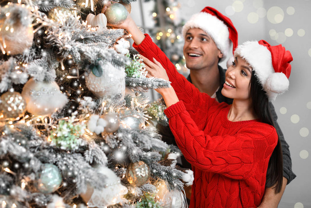 Happy young couple in Santa hats decorating Christmas tree toget - Photo, Image