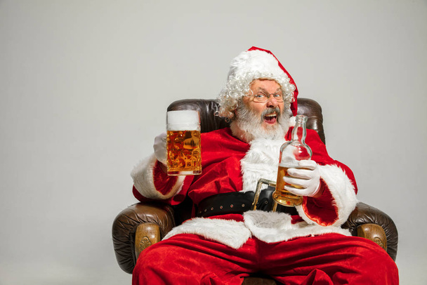 Santa Claus drinking beer sitting on armchair, congratulating of New Year 2020 - Fotó, kép