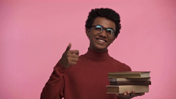 Афріканський підліток вказує пальцем на книжки ізольовані на рожевому - Кадри, відео