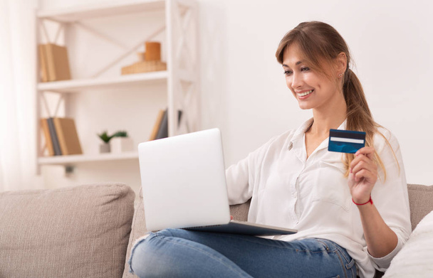 Счастливая женщина держит кредитную карту, совершая покупки дома
 - Фото, изображение