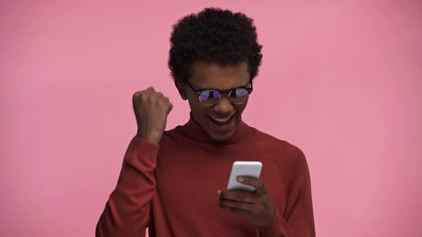 afrykański amerykański nastolatek za pomocą smartfona izolowane na różowy - Materiał filmowy, wideo