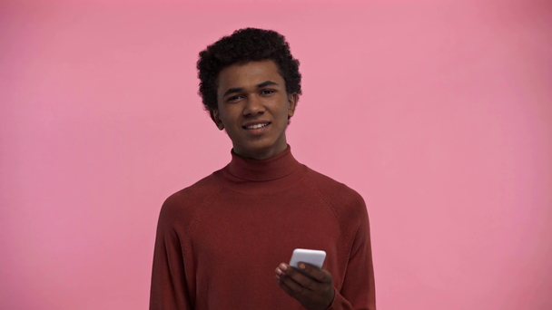 african american teenager using smartphone isolated on pink - Video, Çekim