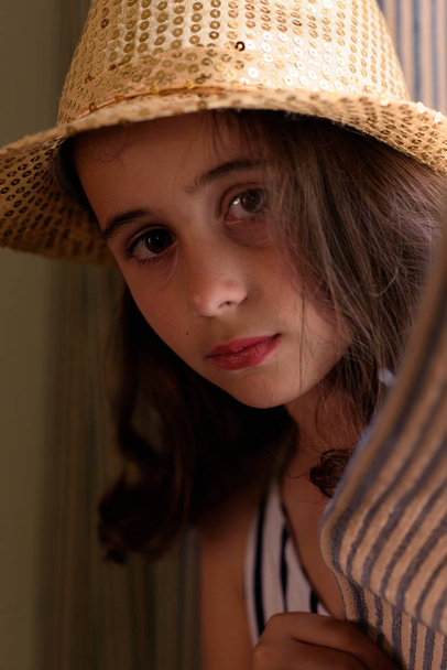 Close-up de menina com cabelo castanho posando com um chapéu dourado
 - Foto, Imagem