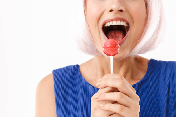 Cropped portrait of young surprised woman wearing pink wig holding lollipop and laughing at camera - Photo, image