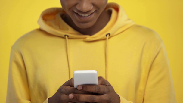 καλλιεργημένη άποψη της αφρικανικής Αμερικανός έφηβος χρησιμοποιώντας smartphone απομονώνονται σε κίτρινο - Πλάνα, βίντεο