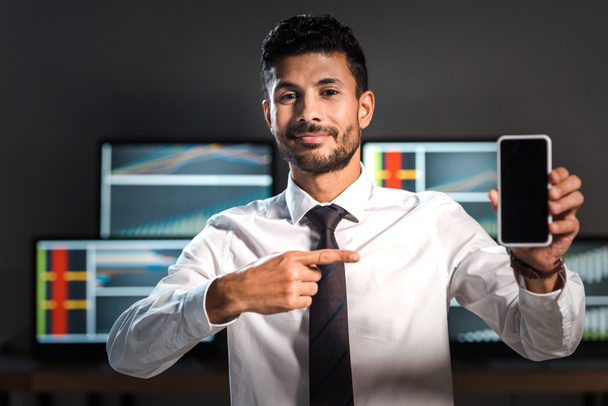 smiling bi-racial trader pointing with finger at smartphone with copy space  - Photo, image