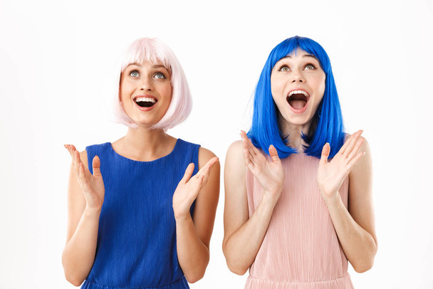 Portrait of two ecstatic women wearing blue and pink wigs looking upward at copyspace - Photo, Image