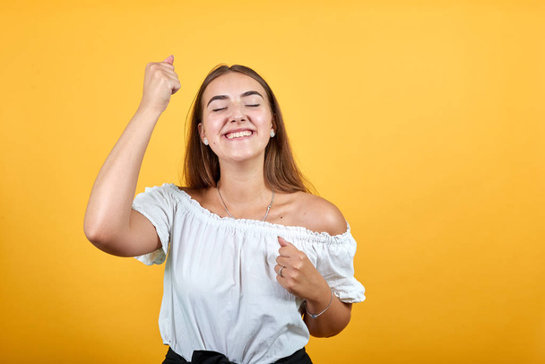 Happy caucasian young woman dancing, keeping fists up, smiling - Фото, изображение