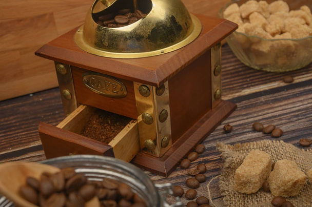 Holzlöffel im Glas mit Kaffeebohnen, Kaffeemühle, braunem Zucker auf Holzgrund. Nahaufnahme. - Foto, Bild