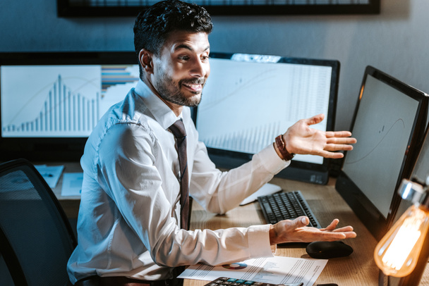 smiling bi-racial trader looking at computer with graphs in office  - Photo, Image
