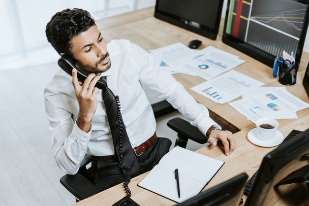 high angle view of bi-racial trader talking on telephone and sitting near computer with graphs  - Foto, immagini