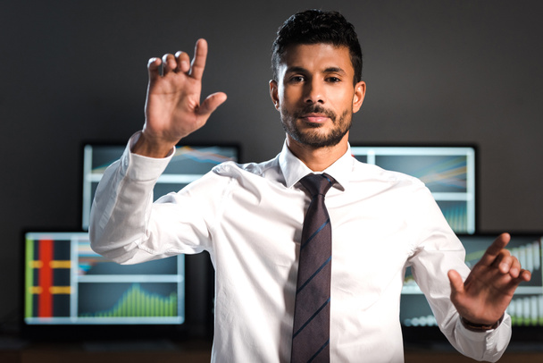 selective focus of bi-racial trader pointing with fingers and computers on background  - Foto, imagen