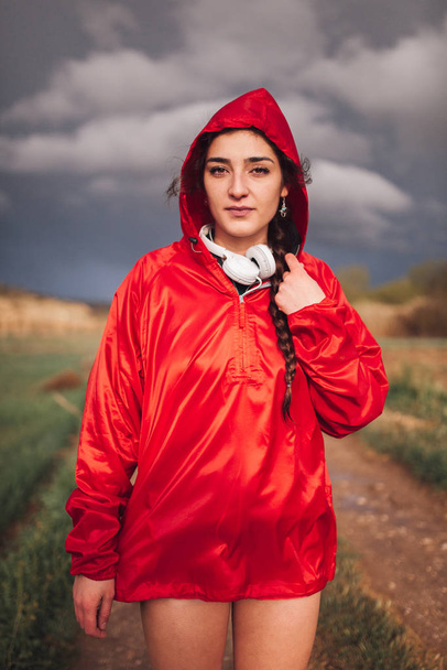 Jonge vrouw met regenjas en koptelefoon op het veld - Foto, afbeelding