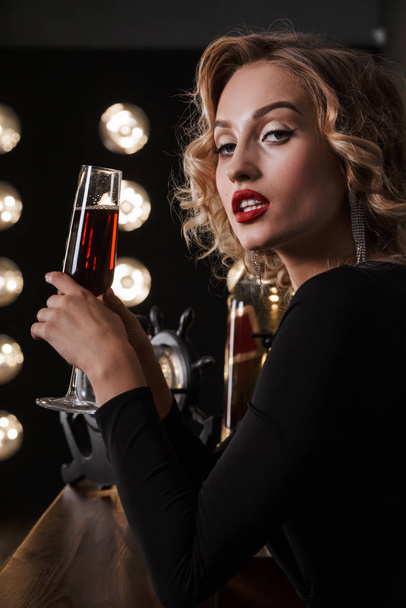 Image of young blonde woman wearing elegant dress drinking red wine - Foto, imagen