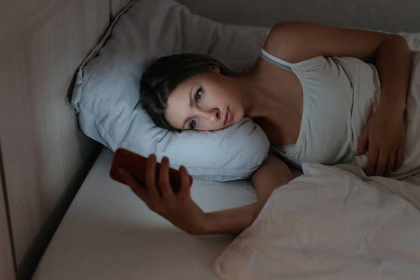 Female using her smartphone in bed at night instead sleeping. - Photo, Image