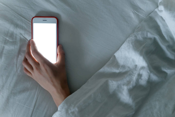 Smartphone που βρίσκεται στο χέρι του κοιμάται θηλυκό κάτω από κουβέρτα. - Φωτογραφία, εικόνα