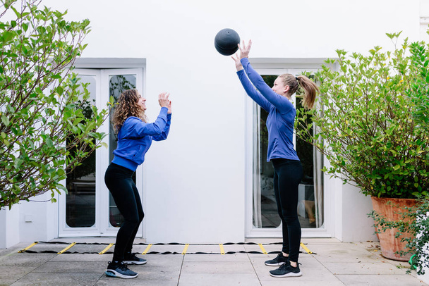 Kaksi nuorta naista tekee liikuntaa yhdessä lääkepallon kanssa
 - Valokuva, kuva
