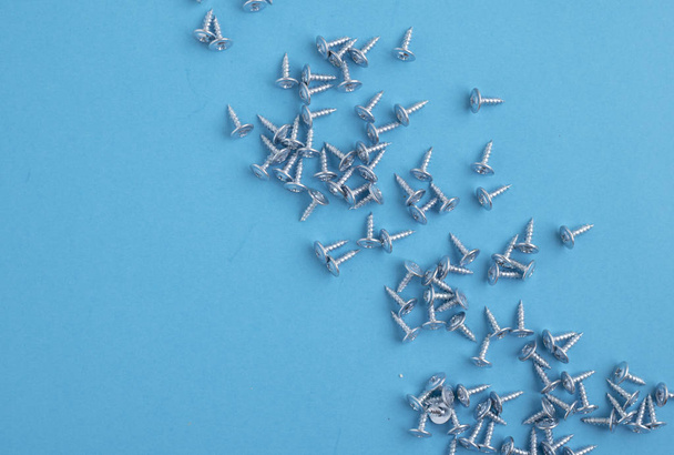 Many screws on blue paper, blurred background - Foto, afbeelding