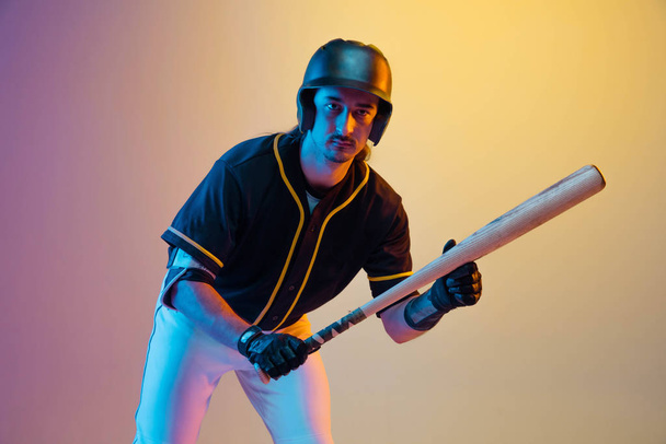 Baseball player, pitcher in a black uniform practicing on gradient background in neon light - Foto, imagen