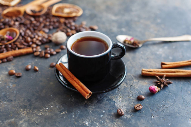 Šálek aromatické černé kávy se skořicovou tyčinkou na talíři, americano nebo espresso. Přísady kávy v pozadí. Tmavý texturovaný kreativní povrch. Zavřít, selektivní zaměření. - Fotografie, Obrázek
