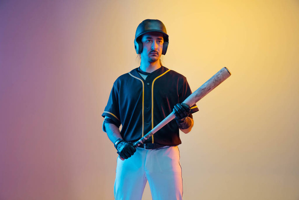 Beyzbol oyuncusu, siyah üniformalı atıcı neon ışıklı arka planda pratik yapıyor. - Fotoğraf, Görsel
