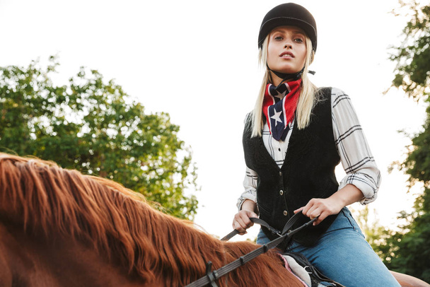 Image of pretty woman wearing hat riding horse at yard in countr - Foto, imagen